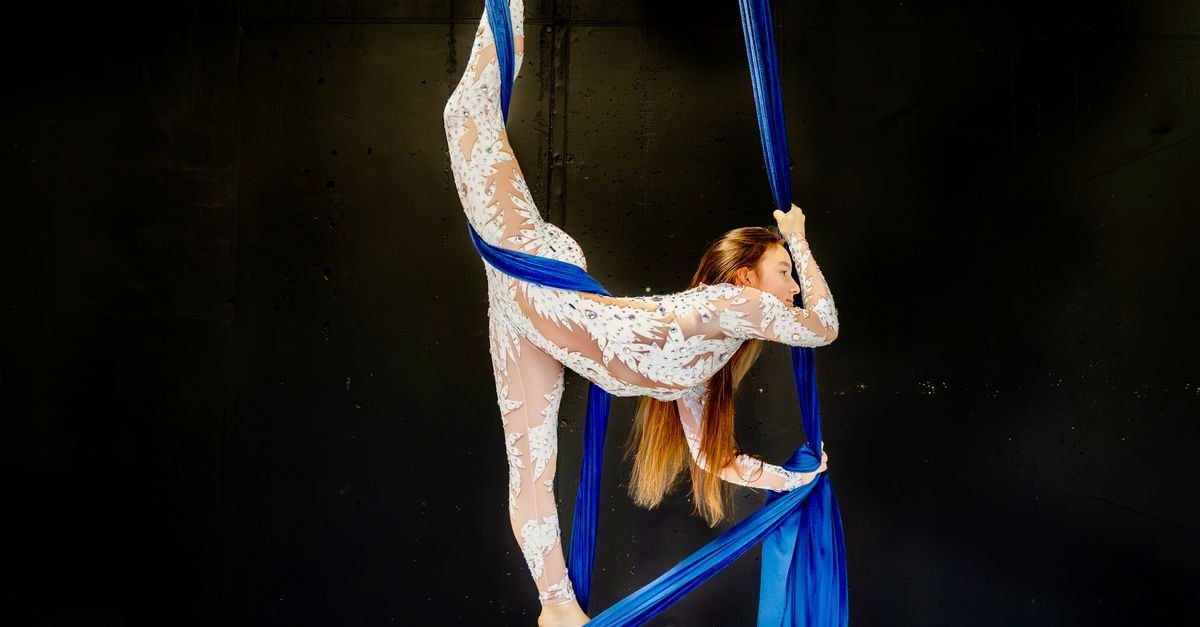 Artista circense em número de tecido acrobático azul contra fundo escuro