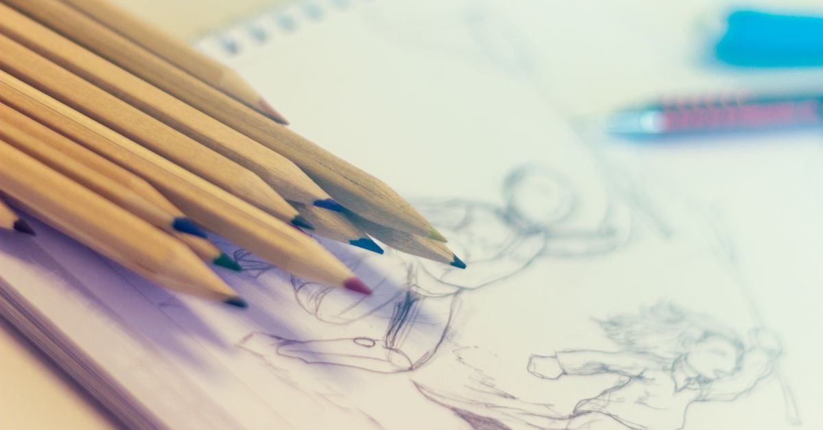Lápis de cor apoiados sobre caderno de desenho com esboços a grafite