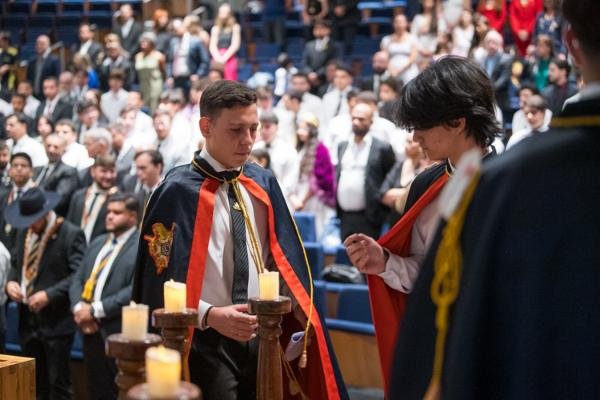 Jovens de capa em cerimônia da Ordem DeMolay no plenário da Câmara Legislativa, com velas acesas