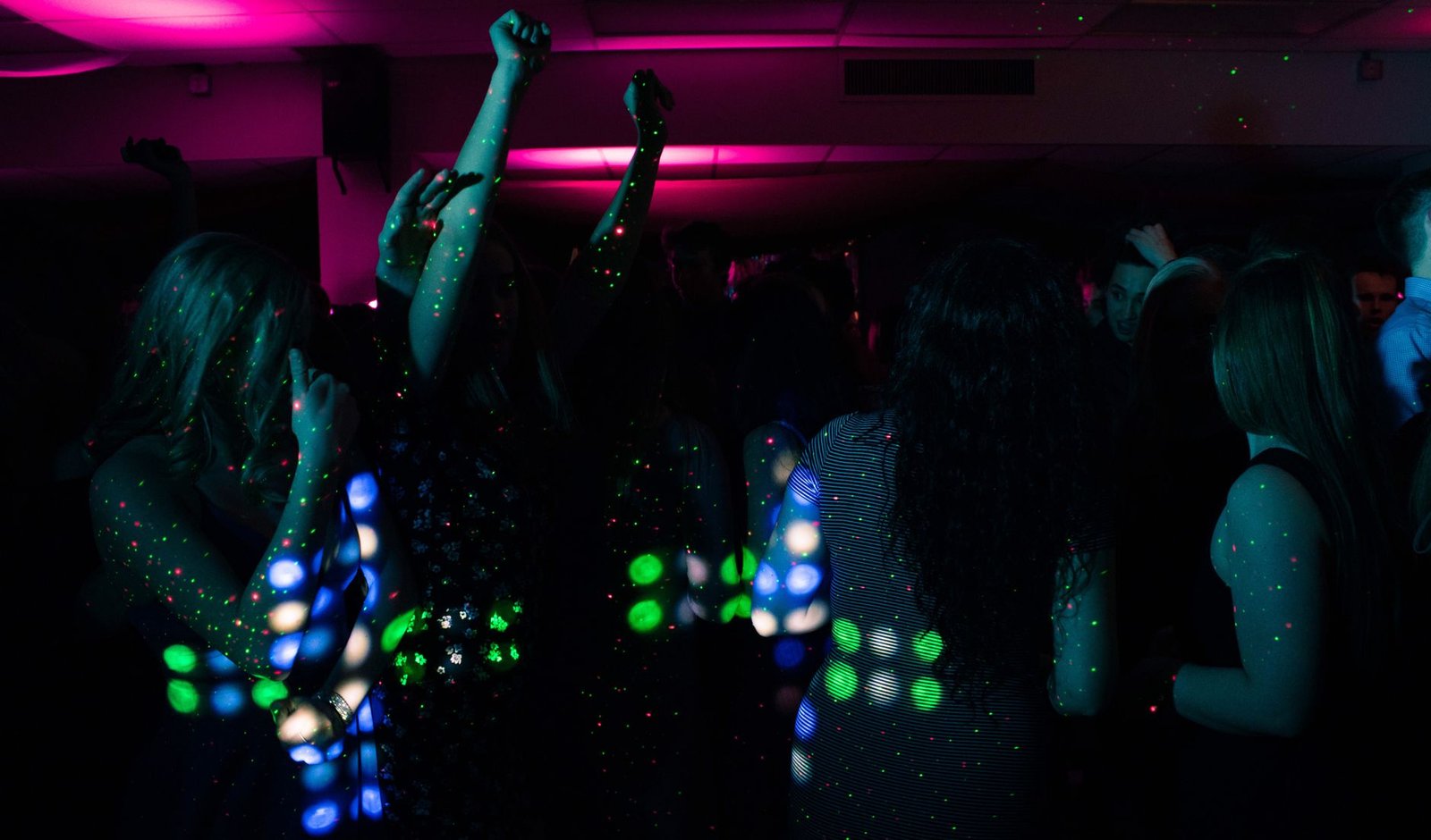 Pessoas dançando em salão escuro com luzes coloridas de festa