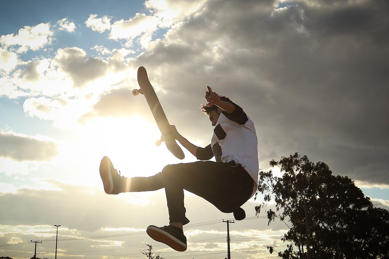 Skatista salta com o skate no ar, em contraluz, sob céu com nuvens