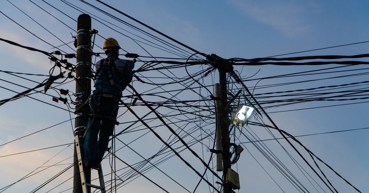 Eletricista com capacete trabalha em poste da rede elétrica ao entardecer