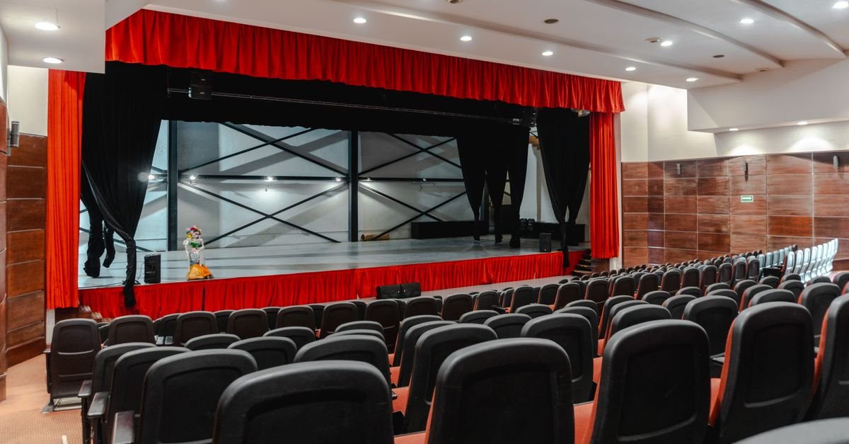 Palco de teatro com cortina vermelha e plateia vazia