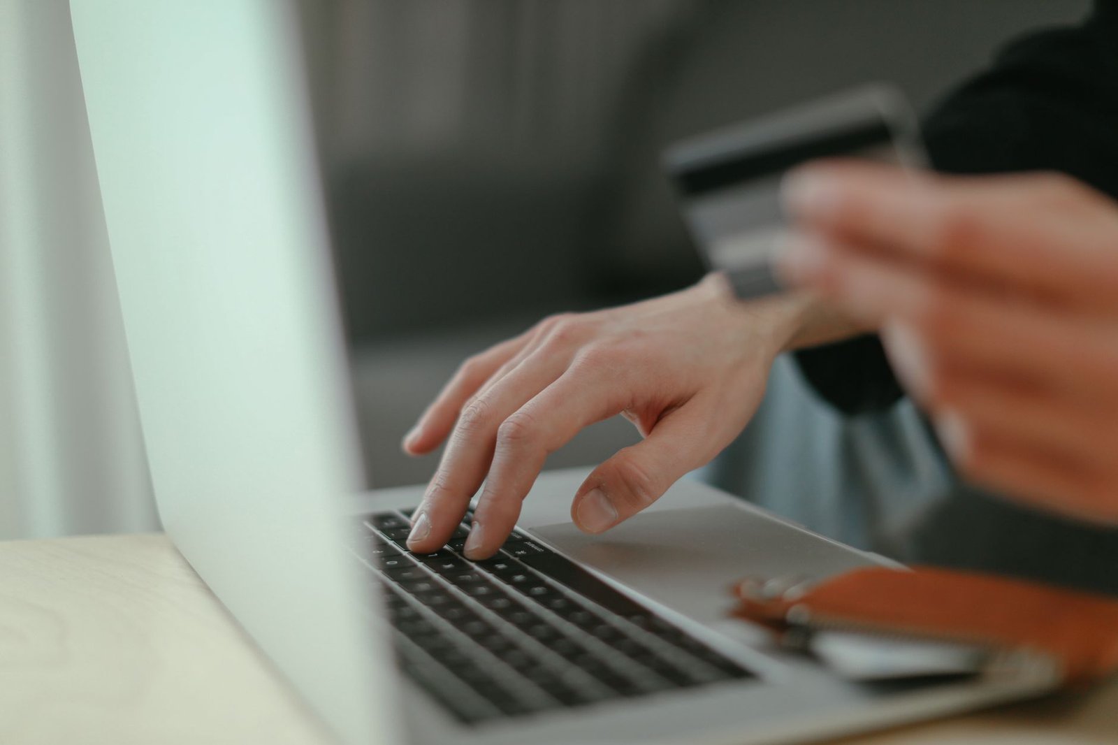 Mãos de uma pessoa digitando em um notebook enquanto seguram um cartão de crédito