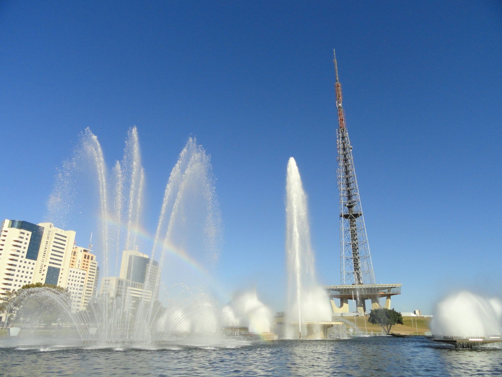 Jatos da fonte luminosa e arco-íris diante da Torre de TV de Brasília, sob céu azul