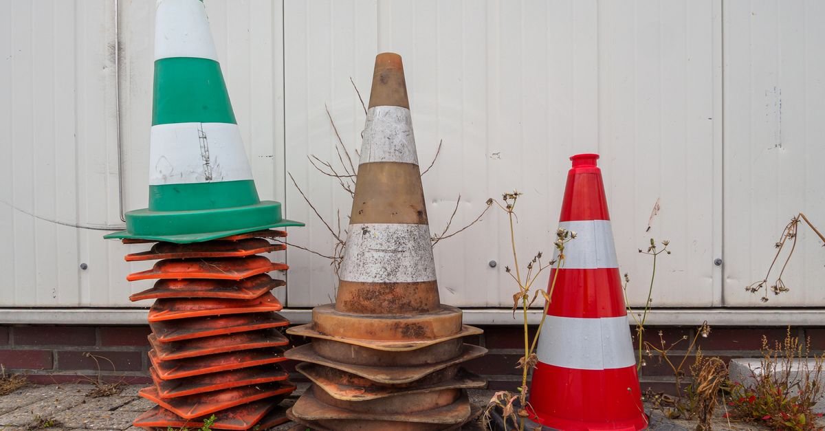 Cones de trânsito de diferentes cores apoiados e empilhados junto a um muro