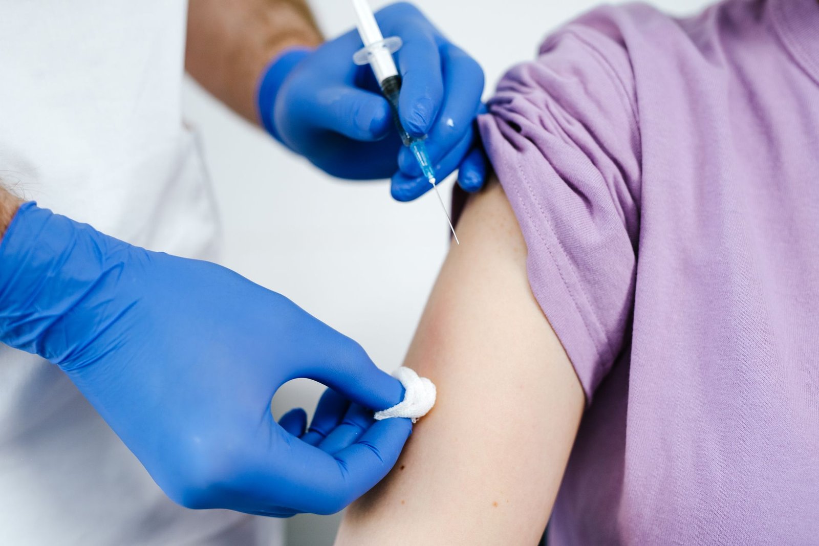 Profissional de saúde com luvas azuis aplica vacina no braço de uma pessoa