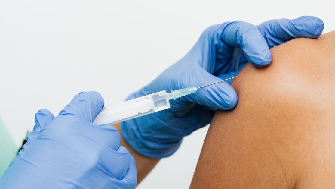 Profissional de saúde com luvas azuis aplicando vacina no braço de um paciente