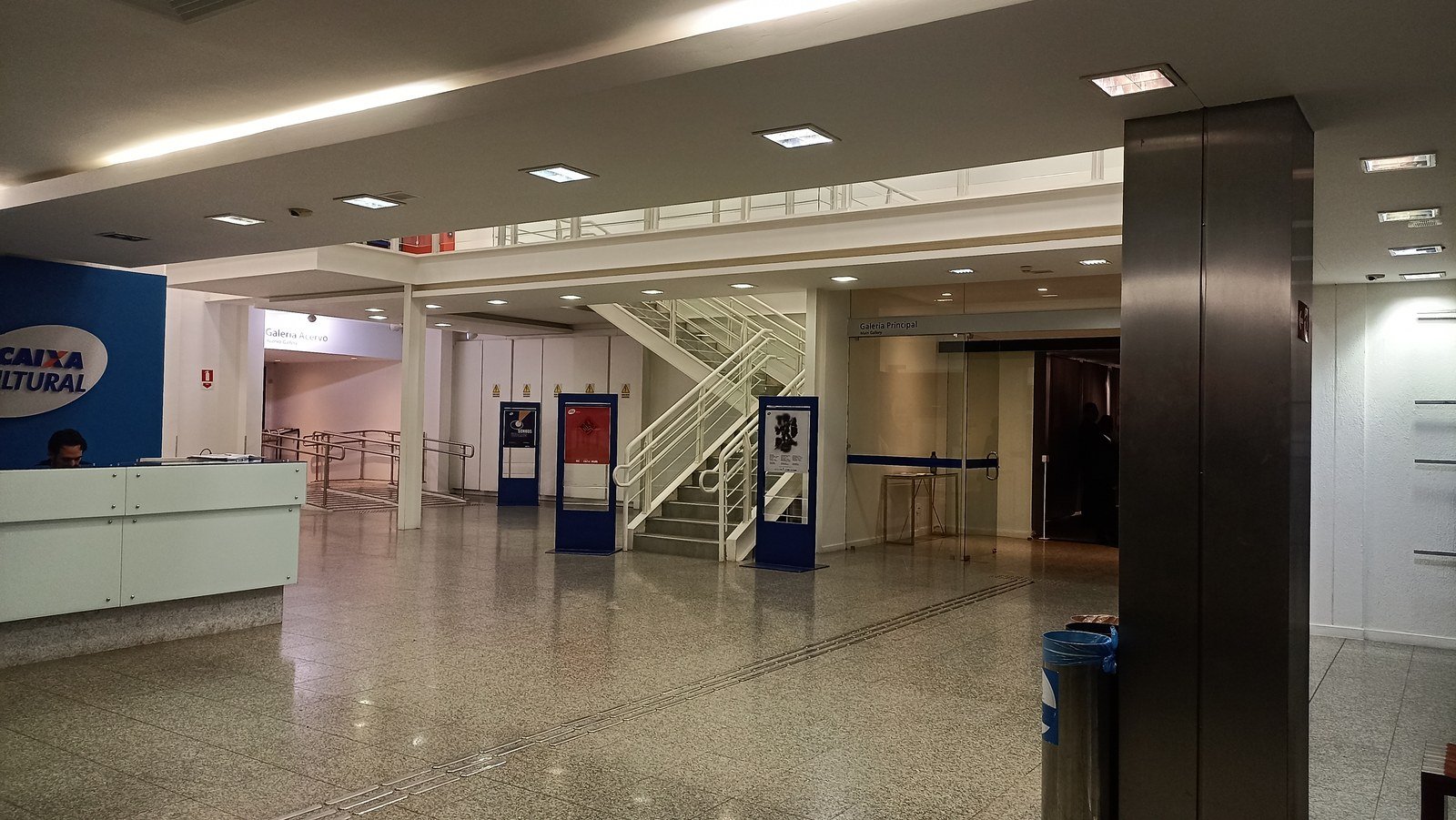 Saguão da Caixa Cultural Brasília, com balcão de recepção e escada ao fundo